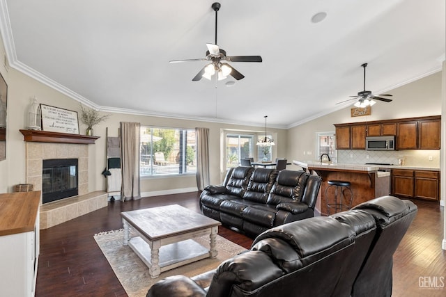 living room with a tile fireplace, lofted ceiling, ornamental molding, ceiling fan, and dark wood-type flooring