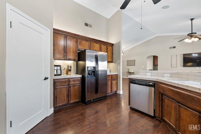 kitchen with tile countertops, appliances with stainless steel finishes, dark hardwood / wood-style flooring, ceiling fan, and backsplash