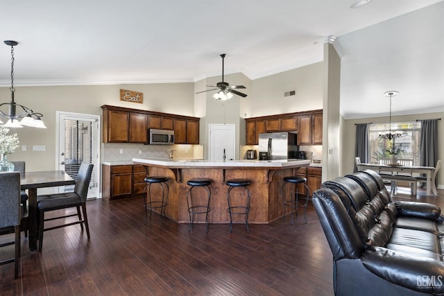 kitchen with a breakfast bar area, dark wood-type flooring, stainless steel appliances, a center island, and decorative light fixtures