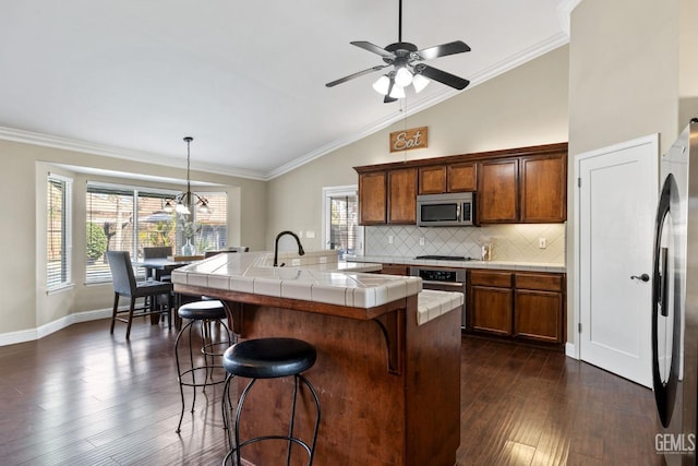 kitchen with appliances with stainless steel finishes, tile countertops, decorative light fixtures, an island with sink, and a kitchen bar