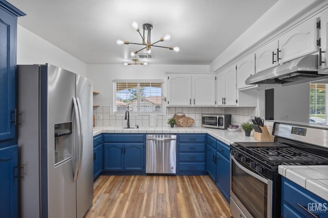 6418 Abby Rose Ave, Bakersfield, CA 93308 - kitchen featuring stainless steel appliances, a sink, under cabinet range hood, blue cabinetry, and a chandelier
