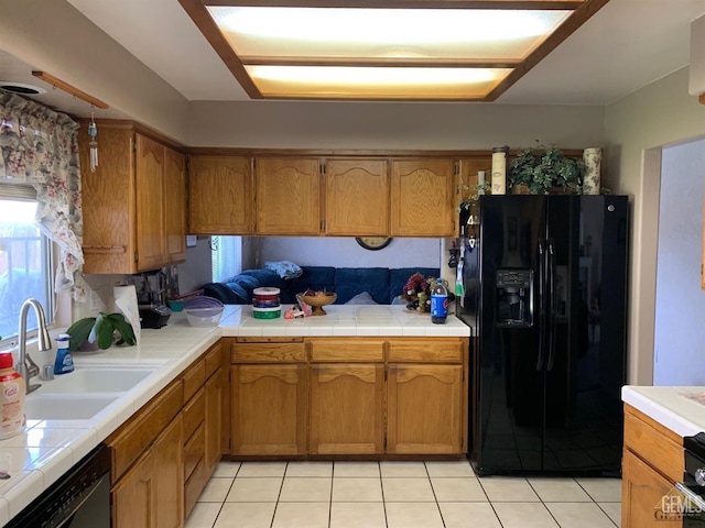 kitchen featuring sink, tile counters, light tile patterned floors, and black appliances