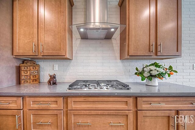 11022 Irontooth Ave, Bakersfield, CA 93311 - kitchen featuring stainless steel gas stovetop, exhaust hood, backsplash, brown cabinetry, and dark stone counters