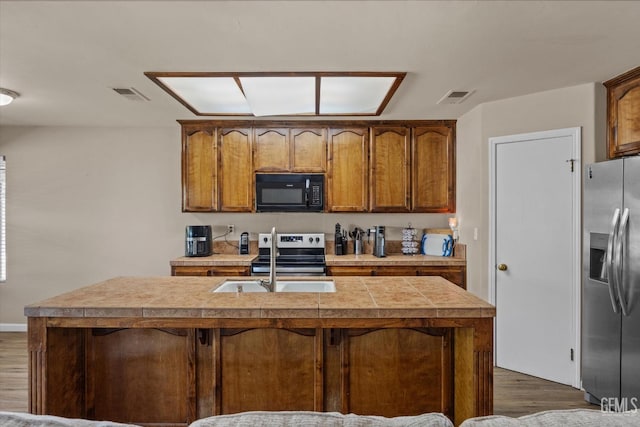 5502 Veneto St, Bakersfield, CA 93308 - kitchen with appliances with stainless steel finishes, dark wood-style flooring, tile countertops, and a center island with sink