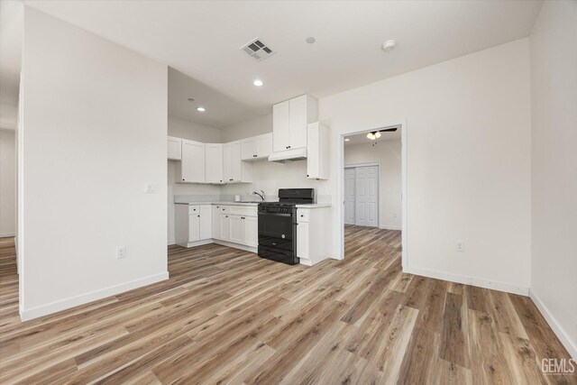 135 L St, Bakersfield, CA 93304 - kitchen featuring black gas range oven, under cabinet range hood, light wood-style floors, light countertops, and white cabinetry