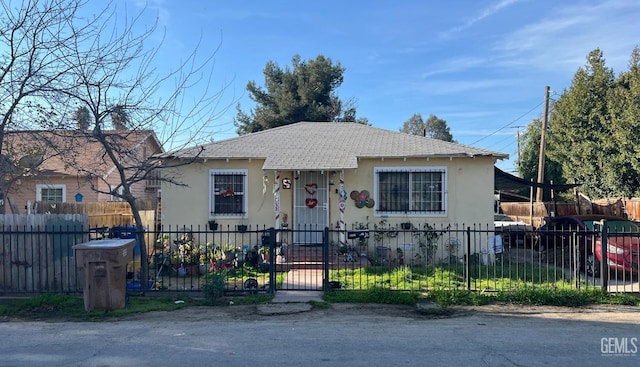 bungalow-style house featuring a shingled roof, a fenced front yard, and stucco siding