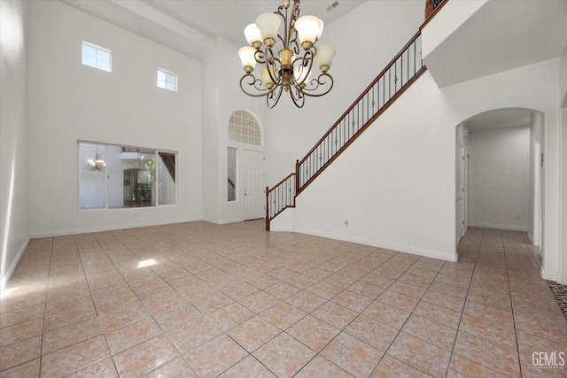 unfurnished living room featuring light tile patterned flooring, arched walkways, a chandelier, baseboards, and a towering ceiling