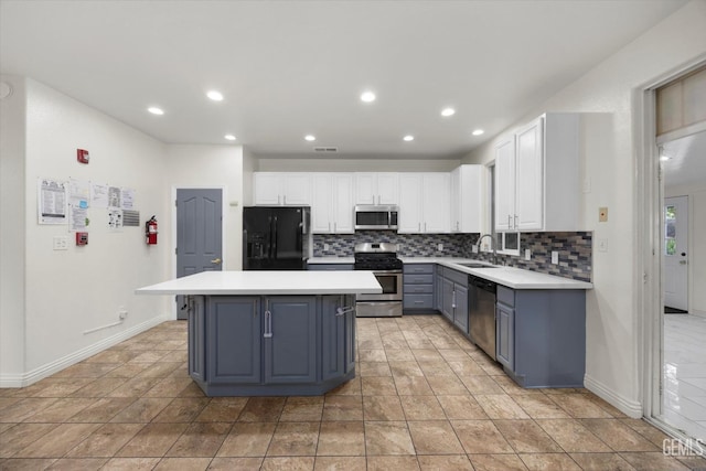 kitchen featuring a kitchen island, tasteful backsplash, a sink, white cabinets, and stainless steel appliances