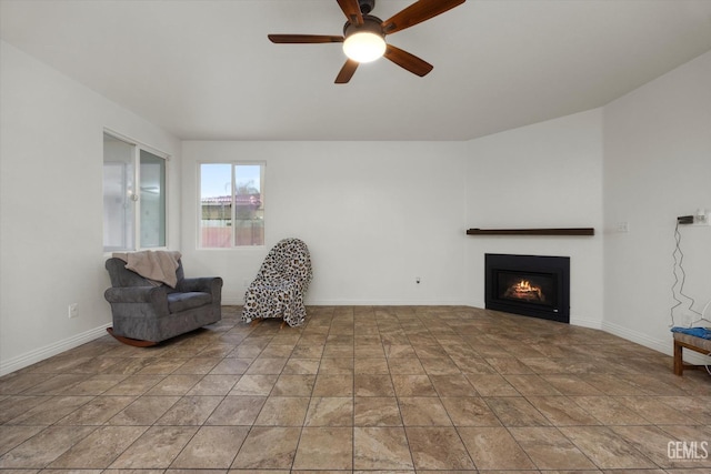 living area featuring stone finish floor, baseboards, a ceiling fan, and a warm lit fireplace