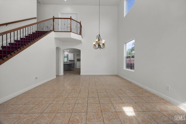 interior space featuring an inviting chandelier, tile patterned flooring, arched walkways, baseboards, and a towering ceiling