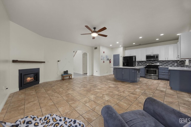 living area with a glass covered fireplace, baseboards, ceiling fan, recessed lighting, and arched walkways