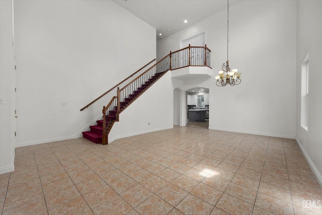 unfurnished living room featuring a towering ceiling, baseboards, tile patterned floors, arched walkways, and a notable chandelier