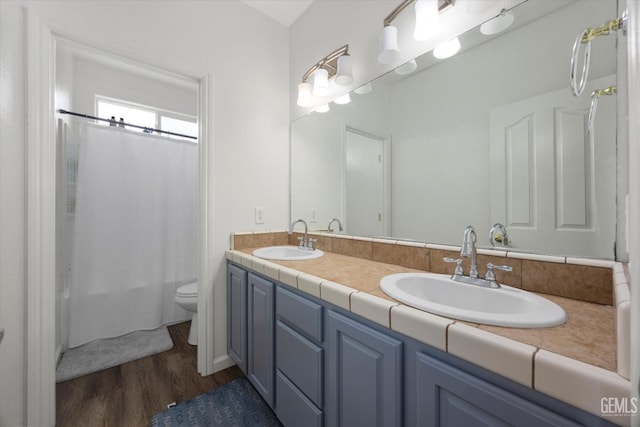 bathroom featuring double vanity, a sink, wood finished floors, and toilet