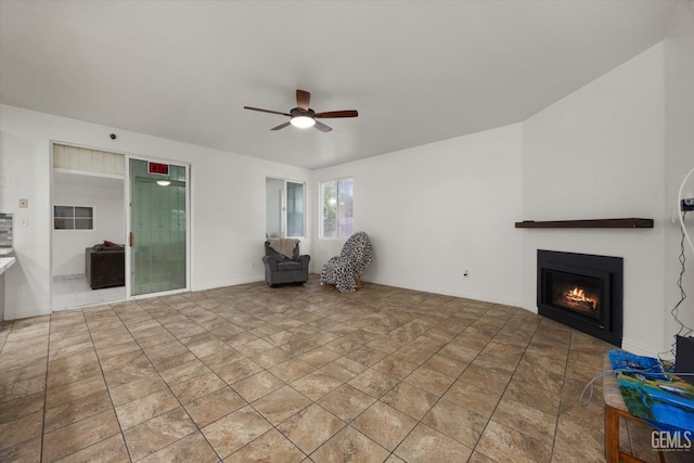 unfurnished living room with baseboards, a ceiling fan, a warm lit fireplace, and stone finish floor