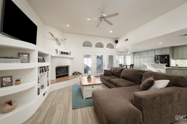 living room with light wood-style floors, visible vents, a ceiling fan, and a glass covered fireplace