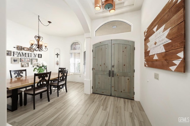 entryway featuring a chandelier, arched walkways, and light wood finished floors