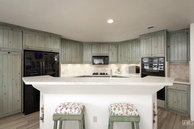 kitchen featuring light wood-type flooring, black appliances, light countertops, and gray cabinetry