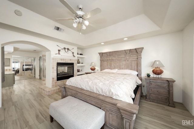 bedroom featuring light wood-style flooring, a tiled fireplace, visible vents, and a tray ceiling