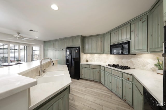 kitchen with tasteful backsplash, light countertops, visible vents, a sink, and black appliances