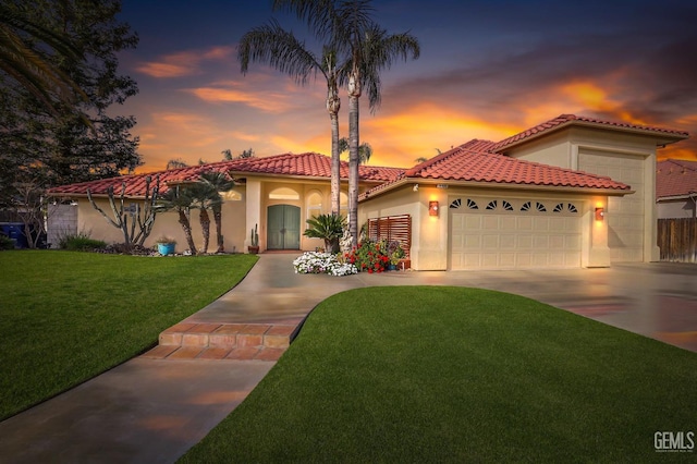 mediterranean / spanish-style home featuring concrete driveway, a yard, an attached garage, and stucco siding