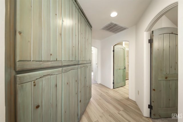 corridor with light wood-style flooring, visible vents, and arched walkways