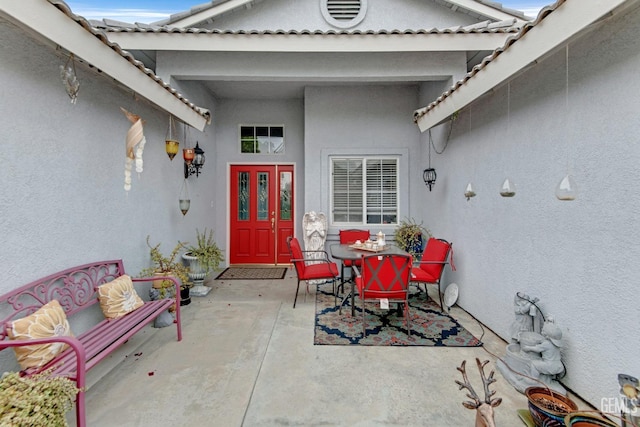 entrance to property with a patio area, stucco siding, a tile roof, and outdoor dining space