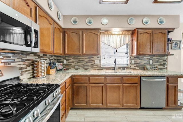 kitchen featuring light stone counters, a sink, brown cabinets, and stainless steel appliances