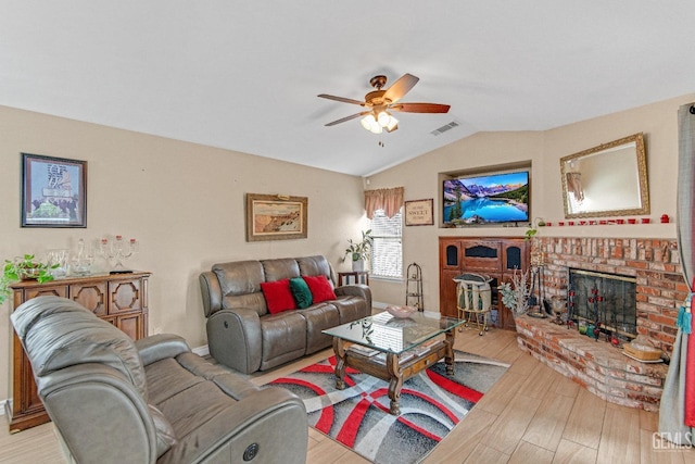 living area featuring a ceiling fan, visible vents, a brick fireplace, wood finished floors, and lofted ceiling