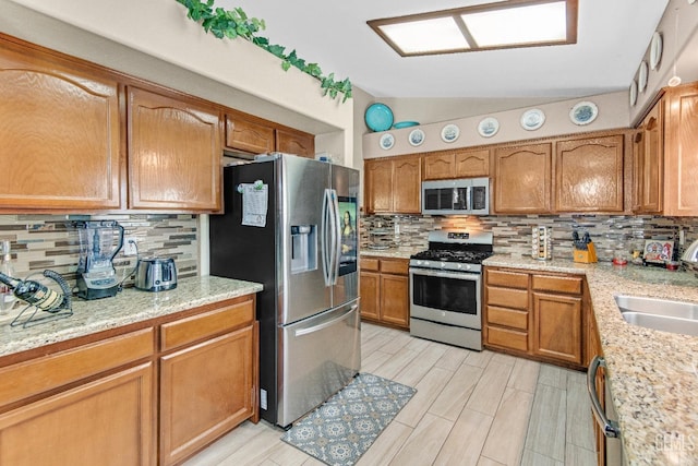 kitchen with a sink, appliances with stainless steel finishes, decorative backsplash, and vaulted ceiling