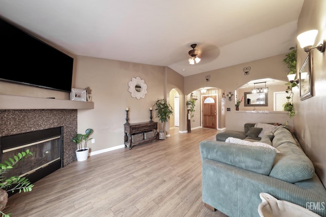 living room featuring ceiling fan, light wood-type flooring, vaulted ceiling, and a tile fireplace