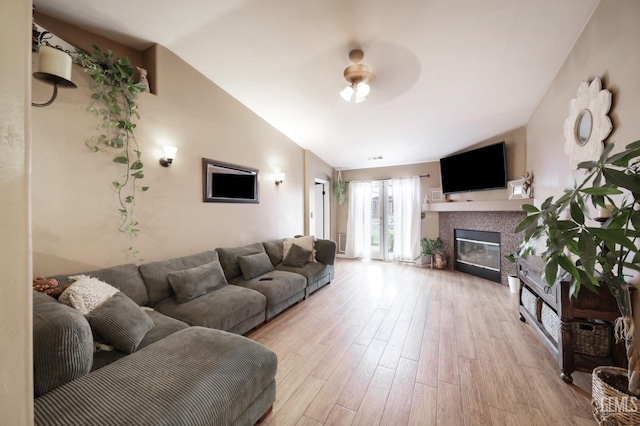 living room featuring light wood-type flooring, vaulted ceiling, and a tile fireplace