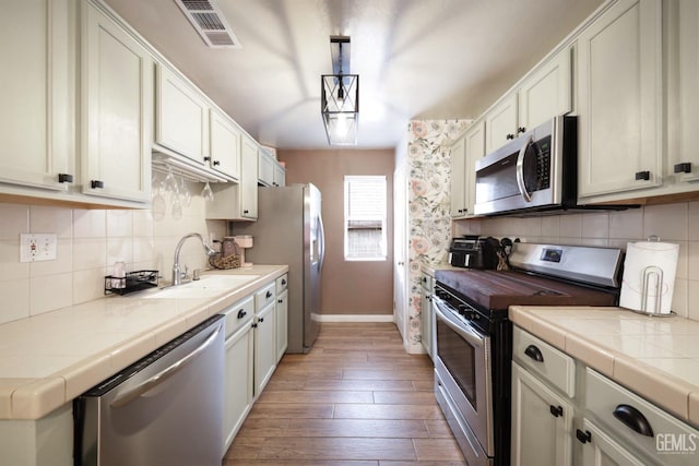 kitchen with appliances with stainless steel finishes, hanging light fixtures, tile countertops, sink, and white cabinetry