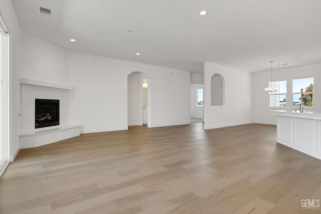 unfurnished living room featuring plenty of natural light, an inviting chandelier, and light hardwood / wood-style floors