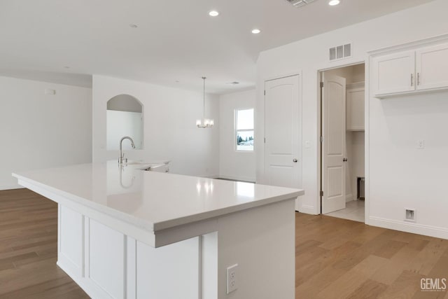 kitchen with white cabinetry, an island with sink, and pendant lighting