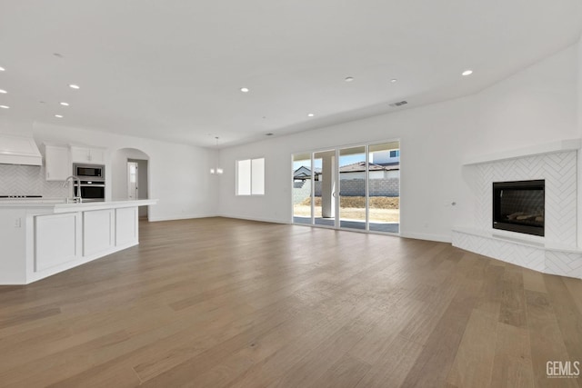 unfurnished living room with a tiled fireplace, sink, and light hardwood / wood-style flooring