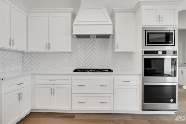 kitchen with white cabinetry, premium range hood, appliances with stainless steel finishes, and tasteful backsplash