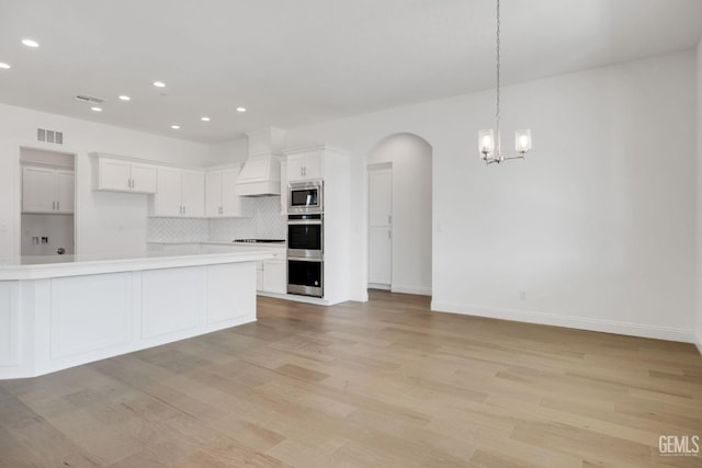 kitchen featuring white cabinetry, decorative backsplash, custom exhaust hood, and appliances with stainless steel finishes