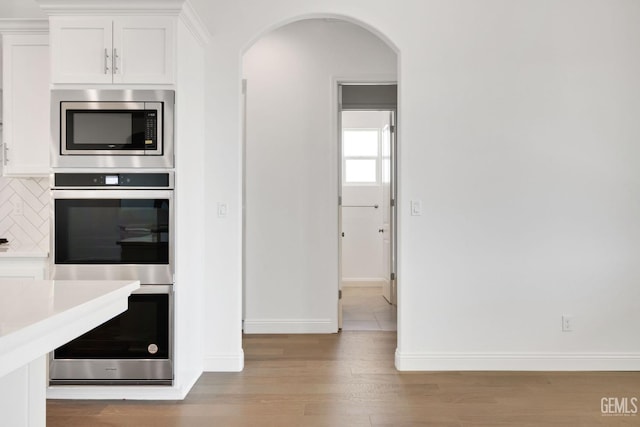 kitchen featuring appliances with stainless steel finishes, light hardwood / wood-style flooring, white cabinets, and decorative backsplash