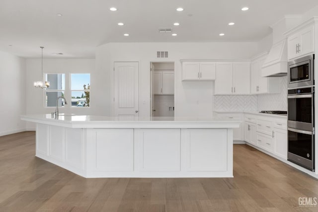 kitchen featuring stainless steel appliances, a center island with sink, and white cabinets