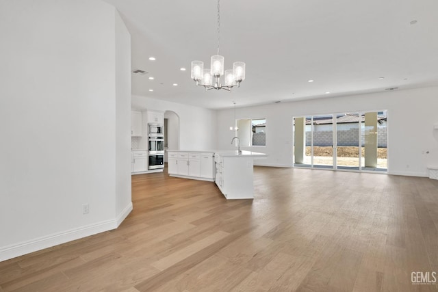 unfurnished living room with sink, light hardwood / wood-style floors, and a chandelier