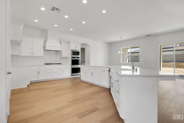 kitchen with premium range hood, a healthy amount of sunlight, stainless steel appliances, and white cabinets