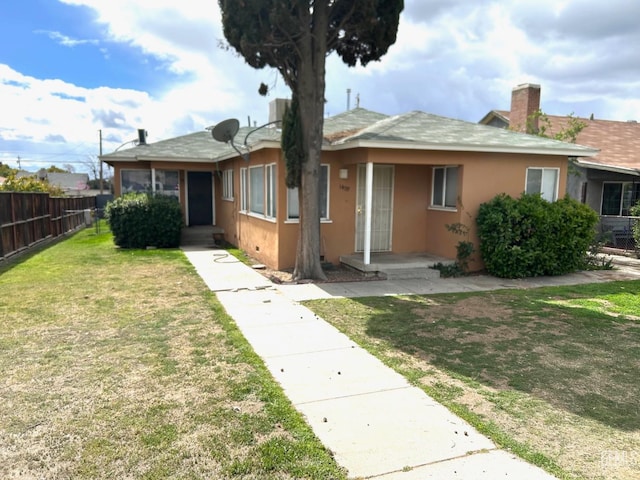 view of front of house featuring fence, a chimney, a front lawn, and stucco siding