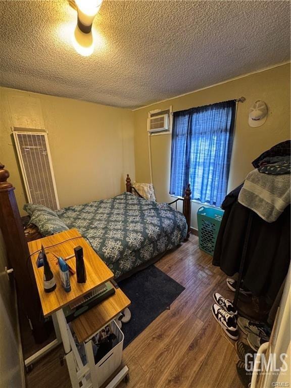 bedroom with a textured ceiling, a wall unit AC, a heating unit, and wood finished floors