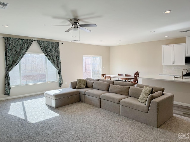 carpeted living room featuring ceiling fan and sink