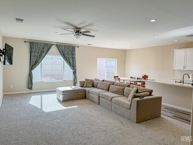 carpeted living room featuring ceiling fan and sink