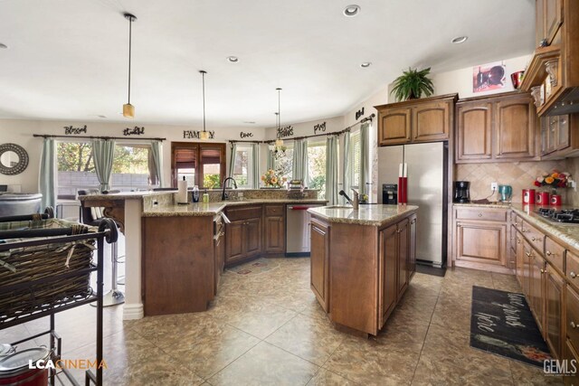 kitchen featuring a kitchen island with sink, sink, hanging light fixtures, light stone countertops, and stainless steel appliances