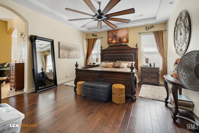 bedroom with ceiling fan, dark hardwood / wood-style flooring, a tray ceiling, and multiple windows