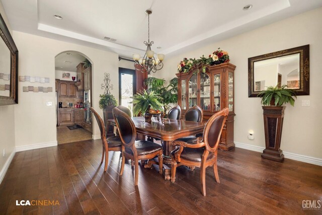 dining space featuring a chandelier, dark hardwood / wood-style flooring, and a tray ceiling