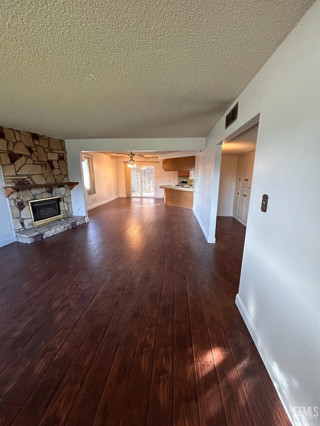 unfurnished living room with dark hardwood / wood-style flooring, ceiling fan, a stone fireplace, and a textured ceiling