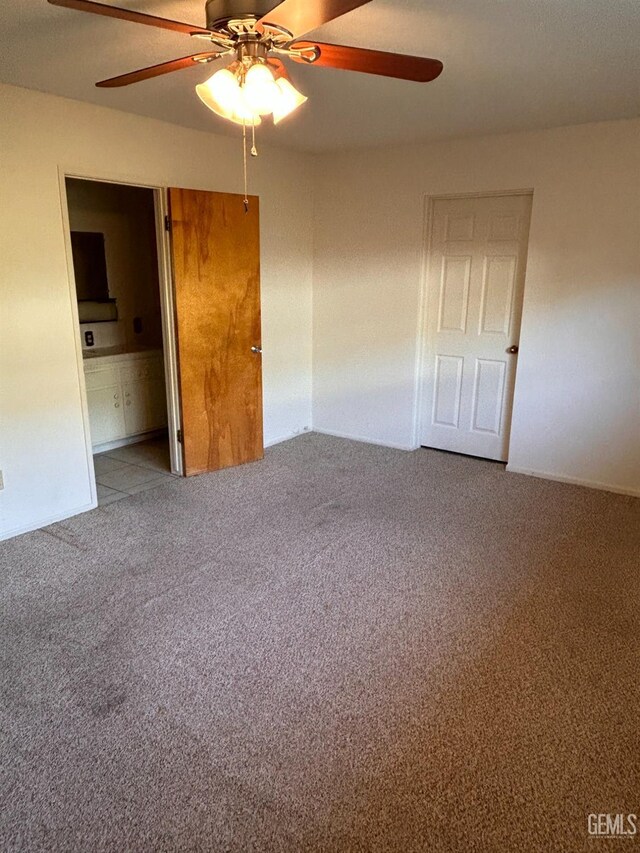 unfurnished bedroom featuring carpet floors, a closet, ensuite bath, and ceiling fan